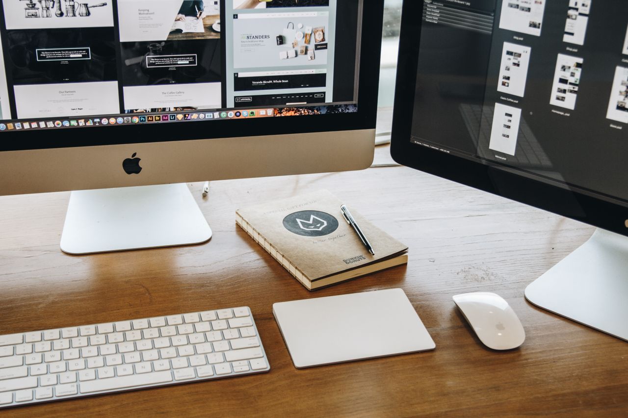 Un espace de bureau minimaliste avec deux écrans, un clavier, une souris et un carnet, pensé pour la productivité.